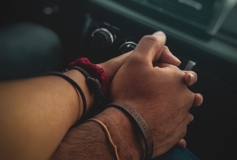 Close up of two individuals holding hands in a car with a blurred stereo in the background